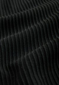 Sort ribbet stof med en blød tekstur, der har skiftende hævede og indtrukne linjer; fibrene virker fine og tæt vævet.