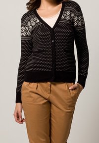 Svart och krämfärgad kofta med V-ringning, knappstängning och geometriska mönster på oket. Tillverkad av stickat tyg med två framfickor.