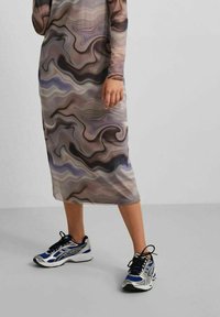 Vestido largo y estampado en tonos beige, marrón y gris con diseños en espiral. Combinado con zapatillas deportivas negras y azules.