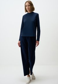 Marineblauwe top met lange mouwen en hoge hals, gecombineerd met marineblauwe wijde broek. Zachte, gestructureerde stof, aangevuld met witte sneakers.