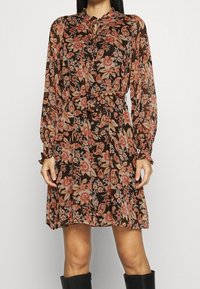 Pitkähihainen, ruskea kukallinen mekko, jossa on istuva vyötärö ja frillahihojen reunat. Mekossa on vaaleanpunaisia ja kermaisia paisley-kuvioita sekä napitettava pääntie.