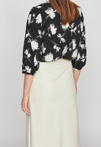 Blusa nera con fantasie floreali bianche, maniche 3/4 e taglio rilassato; abbinata a una gonna midi color crema, che mostra una superficie liscia.