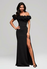 Robe de soirée noire avec manches volantées tombant sur les épaules, corsage ajusté et fente haute, avec un tissu lisse et une coupe longue jusqu'au sol.