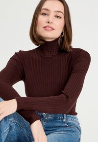 Brun rillede turtleneck sweater med lange ærmer, tætsiddende design og en tekstureret overflade. Kombineret med lys blå højtaljede jeans.