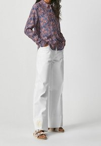 Blommig blus med långa ärmar och rund krage, i marinblått, rosa och vitt. Kombinerad med vida vita byxor och sandaler.