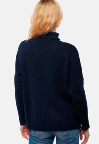 Marineblauer Strickpullover mit hochgeschlossenem Kragen, lockerer Passform und geripptem Saum. Die Textur wirkt weich und dick, ideal zum Schichten.