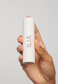 Baume à lèvres ILIA dans un contenant cylindrique blanc, présentant une texture mate lisse et le nom de la marque en relief en gris.