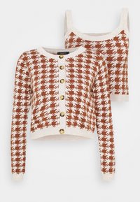 Cardigan en tricot marron et blanc à motif pied-de-poule avec boutons dorés, assorti à un crop top sans manches.