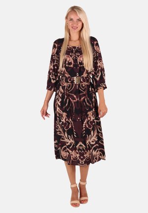 Braun gemustertes Kleid mit Dreiviertelärmeln, tailliertem Schnitt und goldener Gürtelakzent. Getragen mit beigefarbenen Sandalen mit Knöchellriemen.