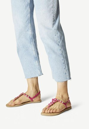 Sandali piatti rosa con un design floreale decorativo, dotati di un post toe e di un cinturino alla caviglia, abbinati a jeans cropped di colore azzurro chiaro.