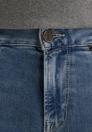 Modré džínsy majú zapínanie na gombík s logom, jemnú textúru odierania a kontrastné oranžové prešívanie pozdĺž švov.