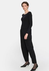 Czarny longsleeve z długim rękawem w połączeniu z czarnymi spodniami typu tapered. Gładki materiał i prosty krój. Uzupełnione czarnymi szpilkami z wąskim noskiem i przezroczystymi czarnymi skarpetkami.