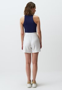 Canottiera a coste blu navy con pantaloni corti bianchi in cotone, caratterizzati da una vita elastica, abbinati a sneakers di colore chiaro.