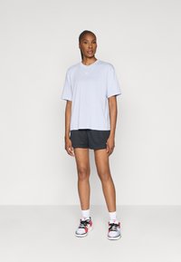 Světle levandulové oversized tričko s jemným logem, spárované s černými síťovinovými šortkami a multifunkčními sportovními botami. Bílé kotníkové ponožky.