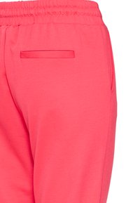 Gros plan sur un pantalon de survêtement à taille élastique rose vif montrant une poche passepoilée à l'arrière et une poche sur la couture latérale.