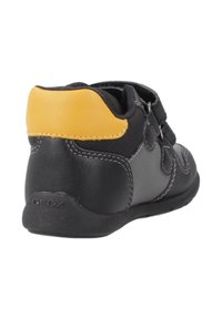 Bottines de sport noires et grises avec un accent jaune au talon, en matériau synthétique, avec deux bandes Velcro et des détails cousus.