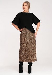 Czarny dzianinowy top z szerokimi rękawami w połączeniu z brązową spódnicą w leopardzie wzory, charakteryzującą się zwiewnym fasonem oraz czarnymi kozakami do kolan.