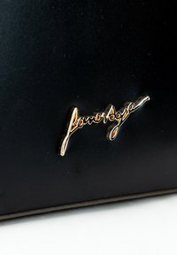 Čierny kožený povrch s prominentne zobrazeným zlatým logom v písanom štýle "floravoge". Textúra je hladká, s minimalistickým dizajnom.