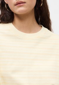 Ανοιχτό κίτρινο φούτερ με ρίγες και μαλακή υφή, διαθέτοντας κλασική ribbed λαιμόκοψη και κοντά μανίκια. Διακοσμητικά στοιχεία περιλαμβάνουν ένα διακριτικό οριζόντιο μοτίβο.