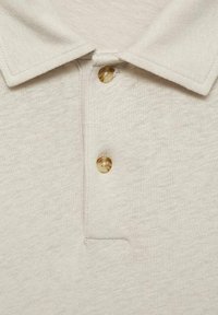 Polo de color beige claro con tejido texturizado, cuello clásico y dos botones de material translúcido.