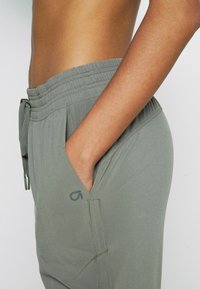 Lichtgroene, lichtgewicht broek met een elastische tailleband, trekkoord en zijzak. Subtiel logo detail bij de zak.