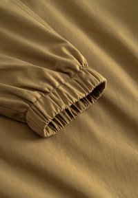 Ruda audinio rankovė su elastiniu rankogaliu, matomas tekstūros ir siūlių raštas ant lygaus audinio.