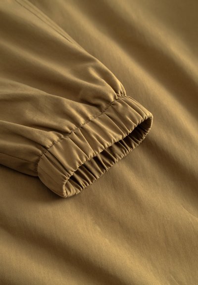 Manche en tissu marron avec détail de poignet élastique, montrant la texture et les coutures sur un matériau lisse.