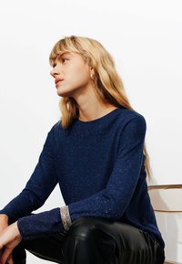 Pull bleu marine avec un col rond, des manches longues et une finition texturée. Associé à un pantalon en cuir noir et un bracelet en argent.