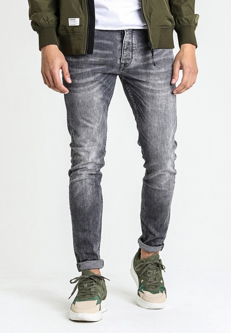 Jeans grises ajustados con un acabado desgastado, que presentan ligeros patrones de desvanecimiento. Combinados con zapatillas verdes y beige, que exhiben cordones texturizados.