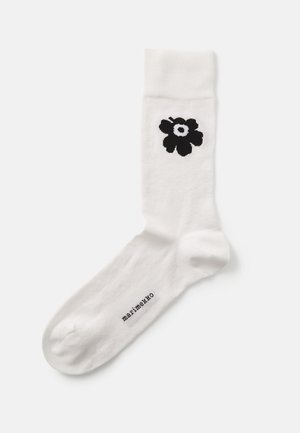 Bijela pamučna čarapa s crnim cvjetnim uzorkom i natpisom "marimekko" otisnutim u crnoj boji blizu prstiju. Glatka tekstura, dužina do sredine lista.