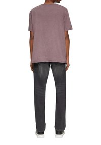 Oversized lavendelkleurig T-shirt met een ronde hals en korte mouwen, gecombineerd met donkergrijze jeans en witte sneakers, gezien vanaf de achterkant.