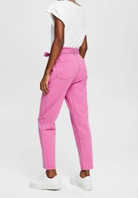 Pantaloni in cotone rosa con vita alta, gamba affusolata e sneakers bianche. Presentano tasche posteriori e una cintura coordinata.