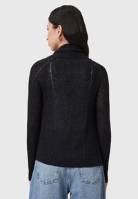 Black ribbed sweater with a high collar and open-knit details at the shoulders, worn with light blue jeans, showing a fitted shape and texture.