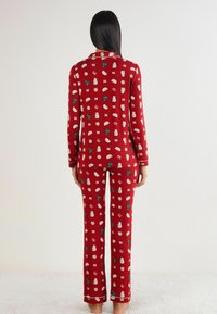 Červený pyžamový set s potiskem vánočních vzorů, včetně stromečků, mašlí a sněhuláků. Měkká tkanina s dlouhými rukávy a kalhotami.