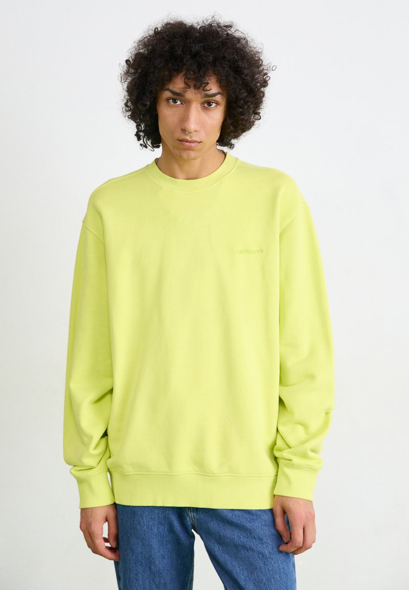 Limegrøn sweatshirt i en afslappet pasform med lange ærmer og ribbede manchetter. Har et diskret logo på brystet. Sammen med blå jeans.