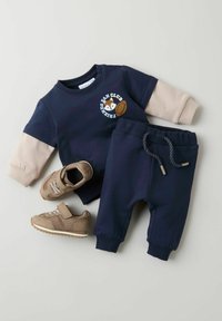 Ensemble pour jeune enfant bleu marine avec des manches beiges, ornée d'un imprimé de renard. Comprend un pantalon assorti et des baskets marron clair avec velcro.