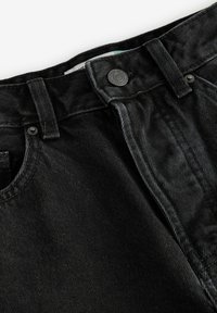 Jeans de mezclilla negra con una superficie texturizada, cierre frontal con botón y diseño clásico de cinco bolsillos con detalles de costura en contraste.