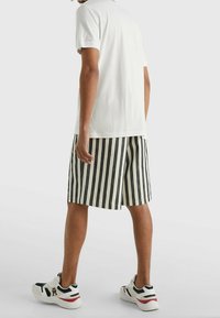 Pruhované bavlněné šortky v černé a bílé barvě s volným střihem, spojené s jednoduchým bílým tričkem a bílými teniskami s akcenty.