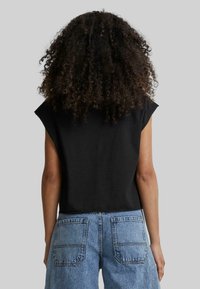 Haut sans manches noir avec une coupe décontractée, fabriqué en coton doux. Associé à un short en denim bleu taille haute avec deux poches arrière.