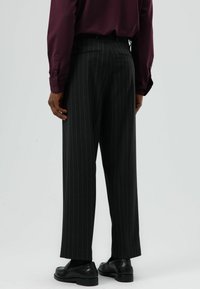 Zwarte pantalon met krijtstreep en een losse pasvorm, voorzien van een platte tailleband en zijzakken, gecombineerd met een bordeauxrode lange mouwen shirt.