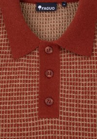 Nahaufnahme eines rostfarbenen und beigen Waffelstrick-Poloshirts mit rostfarbenem Kragen, drei Knöpfen und dem FAGUO Markenlabel in Größe M.