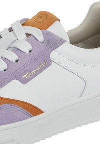 Adidași albi cu accente din suede purpuriu și portocaliu, talpă din cauciuc texturat și șireturi albe. Prezintă un logo auriu pe lateral.