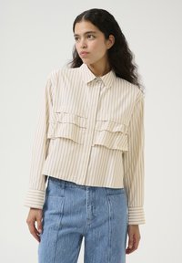Camicia crema con bottoni, a righe verticali blu, dotata di taschini sovrapposti sul petto e maniche lunghe con polsini a righe. Il tessuto appare liscio.