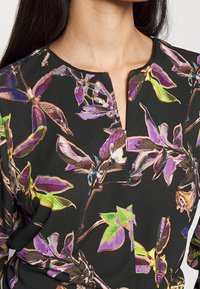 Kleid mit floralem Muster, das lebendige lila und grüne Blätter auf schwarzem Hintergrund zeigt; es hat einen kleinen Reißverschluss vorne und einen runden Ausschnitt.