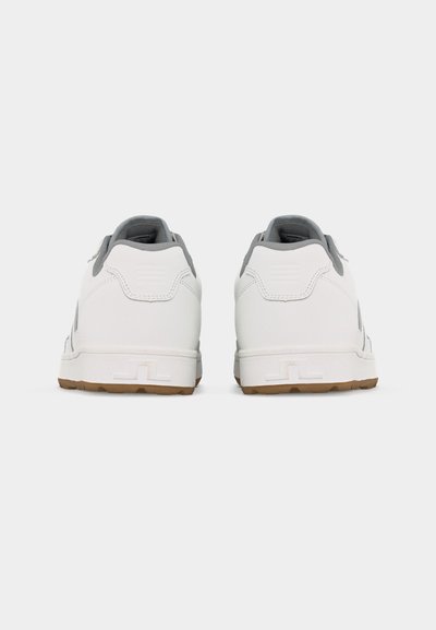 Ζευγάρι λευκά αθλητικά παπούτσια με γκρι εσωτερική επένδυση και σόλες χρώματος καραμέλας, απεικονιζόμενα από πίσω σε απλό ανοιχτό γκρι φόντο.