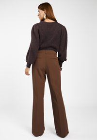 Bruine wollen trui met poffende mouwen, gecombineerd met hoge bruine broeken. De outfit heeft een minimalistisch ontwerp en gladde texturen.