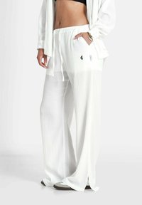 Witte, gekreukte wijde broek met een elastische tailleband, zijzakken en een zwart logo-detail, gemaakt van lichte stof.