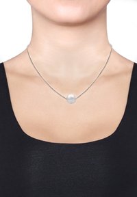 Collier en fil d'argent avec une perle ronde givrée au centre. Design minimaliste, texture lisse et élégance simple contre un haut sombre.