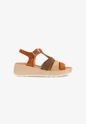 Sandalias de cuña de ante marrón y verde con una correa de tobillo ajustable y una textura parecida a tejido en la suela de color claro.
