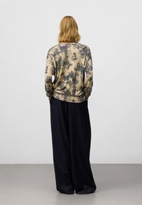 Beige trui met lange mouwen en marineblauwe cirkelpatronen, gecombineerd met losse zwarte broeken. Relaxte pasvorm, zachte textuur die geschikt is voor casual wear.